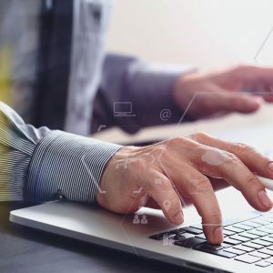 Mãos digitando em notebook com gráficos financeiros na tela