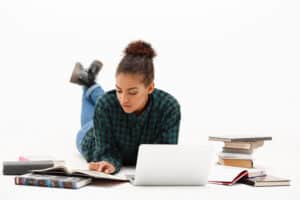 Estudante deitada estudando com notebook e livros