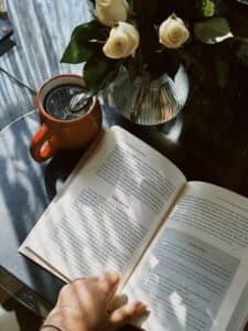 Livro aberto sobre mesa com xícara de café e flores